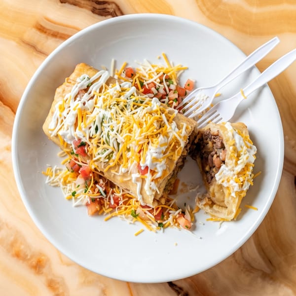 Deep-fried burrito cut in half, topped with cheese, sour cream, and pico de gallo on a white plate.