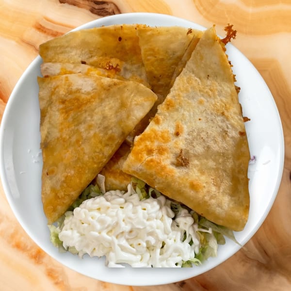 Golden-brown quesadillas, cut into triangles, served on a white plate with shredded lettuce and a dollop of sour cream.