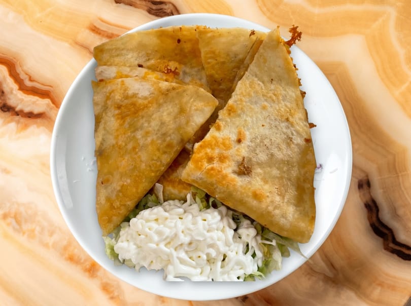 Golden-brown quesadillas, cut into triangles, served on a white plate with shredded lettuce and a dollop of sour cream.