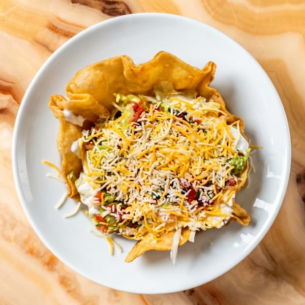 Taco salad in a crispy fried tortilla bowl, topped with cheese, sour cream, and guacamole.