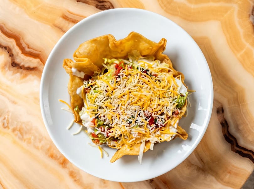 Taco salad in a crispy fried tortilla bowl, topped with cheese, sour cream, and guacamole.