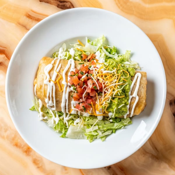 A golden-brown chimichanga topped with sour cream, pico de gallo, guacamole, and shredded cheese.
